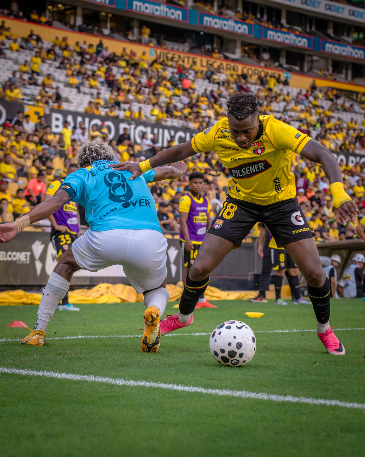 Jugador de Barcelona SC disputa el balón con un futbolista de Universidad Católica junto a la línea lateral del estadio Banco Pichincha.