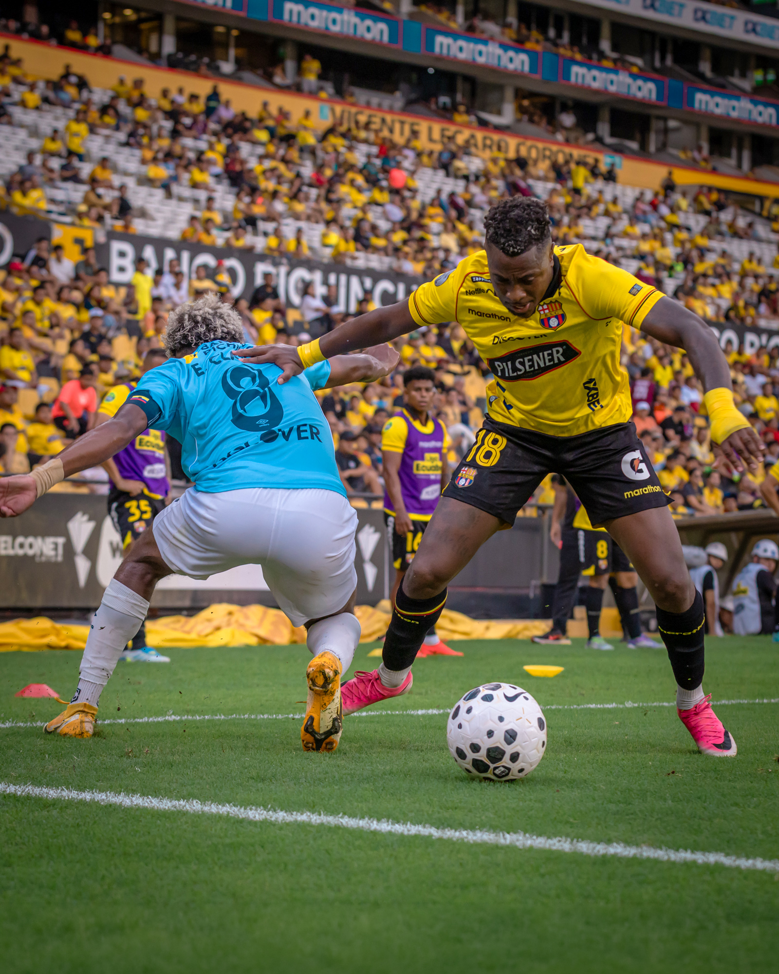 Jugador de Barcelona SC disputa el balón con un futbolista de Universidad Católica junto a la línea lateral del estadio Banco Pichincha.